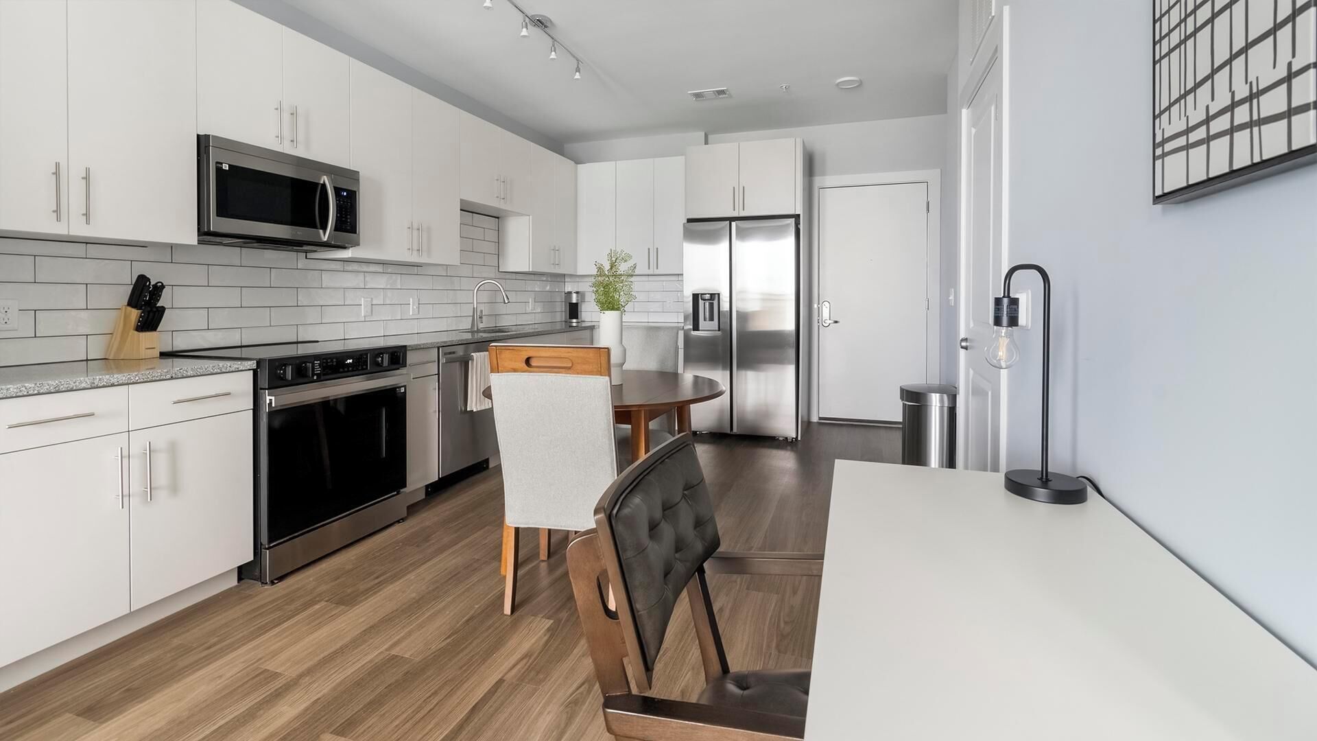 A modern kitchen with white cabinetry, stainless steel appliances, and a wooden dining table.