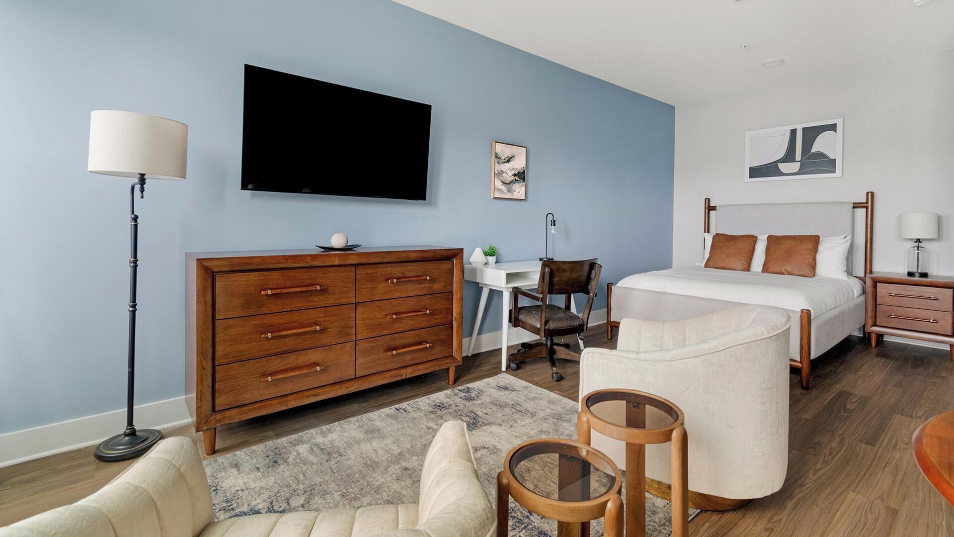 A bedroom with a bed, bedside tables, a desk, a dresser, a TV, and a chair.