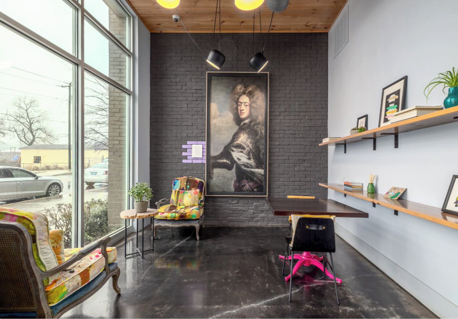 Een modern interieur met een groot raam, een zwarte bakstenen muur, een kleurrijke stoel, een zwart bureau en een roze stoel.