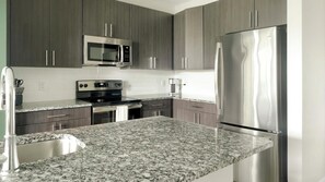 A kitchen with granite countertops, stainless steel appliances, and dark wood cabinets. - Landing | Spectacular 2BD, Gym (Charlotte)