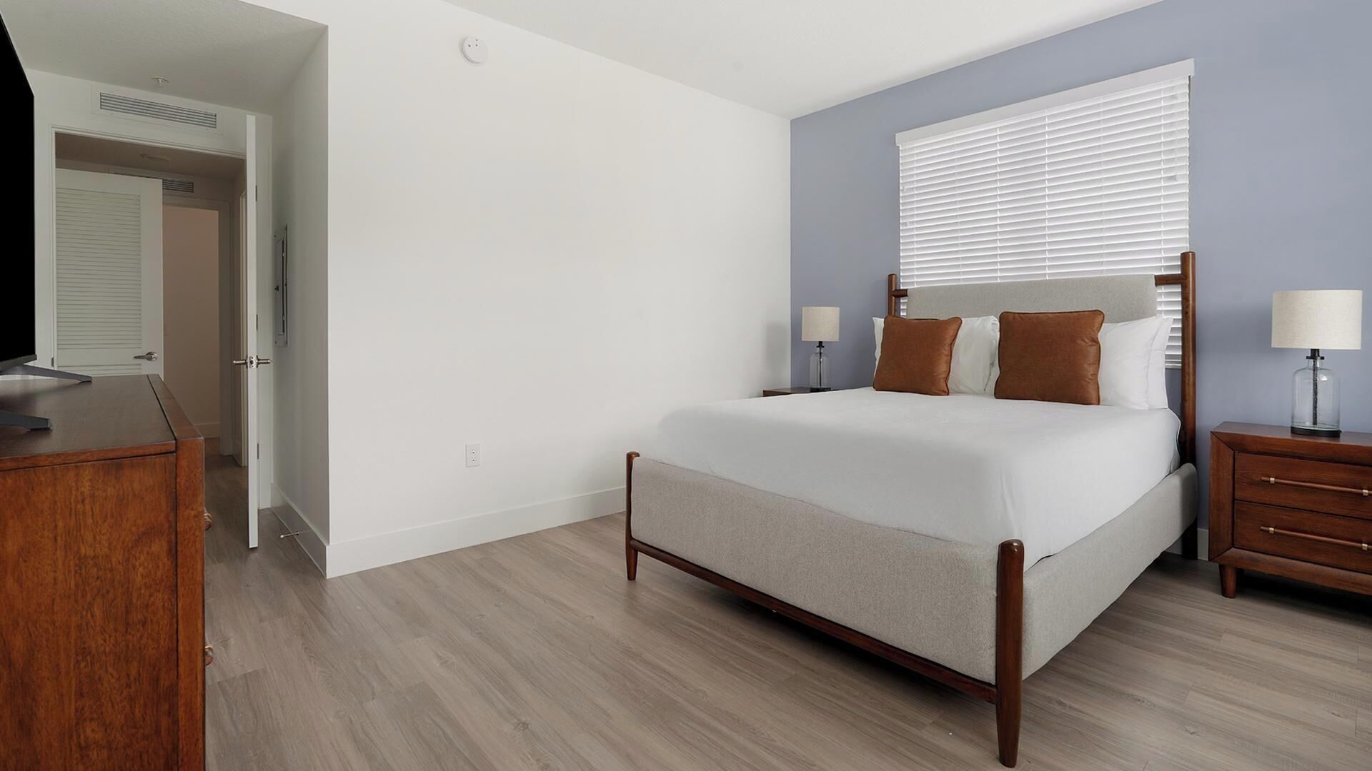Une chambre à coucher comprenant un lit, des tables de chevet, une commode et une fenêtre avec des stores.