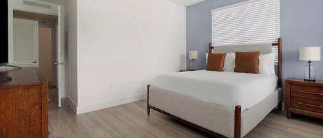 Une chambre à coucher comprenant un lit, des tables de chevet, une commode et une fenêtre avec des stores.