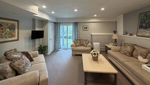 A living room with a sofa, a coffee table, a television, and a door leading to a balcony.