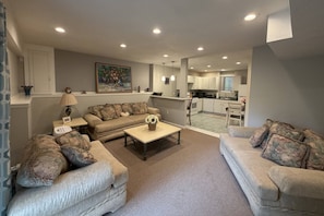 A living room with a sofa set, a coffee table, and a kitchen in the background.