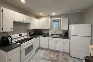 A kitchen with white cabinets, a microwave, a toaster, a coffee maker, and a refrigerator.