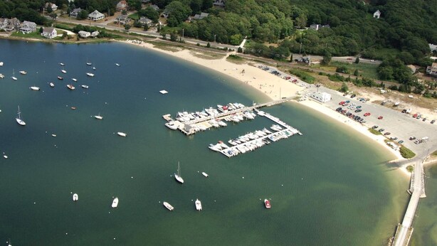 An aerial view of a marina with boats docked, a beach, and surrounding residential areas.