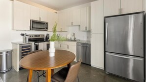 A modern kitchen with stainless steel appliances, a wooden dining table, and white cabinetry. - Landing | Stunning Studio in Kessler Park (Dallas)