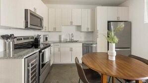 A modern kitchen with stainless steel appliances, a granite countertop, white cabinetry, and a dining area with a wooden table and chairs. - Landing | Stunning Studio in Kessler Park (Dallas)