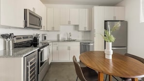 Eine moderne Küche mit Edelstahlgeräten, einer Granitarbeitsplatte, weißen Schränken und einem Essbereich mit Holztisch und Stühlen.