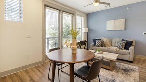 Ein modernes Wohnzimmer mit Essbereich, großen Fenstern, einem Deckenventilator und einer grauen Wand.
