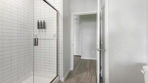 Un baño moderno con paredes de azulejos blancos, cabina de ducha de vidrio y suelo de madera.