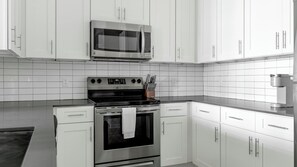 A kitchen with white cabinets, a stainless steel microwave, a stove, and a coffee maker. - Landing | Spectacular 1BD, Gym (Sun City Center)