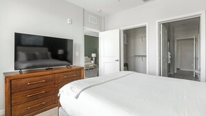 Un dormitorio con televisor en una cómoda, una cama y un armario abierto.