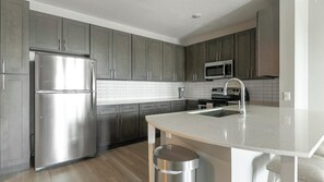 A modern kitchen with grey cabinets, stainless steel appliances, and a central island with a sink. - Landing | Stunning 2BD, Gym (Sun City Center)