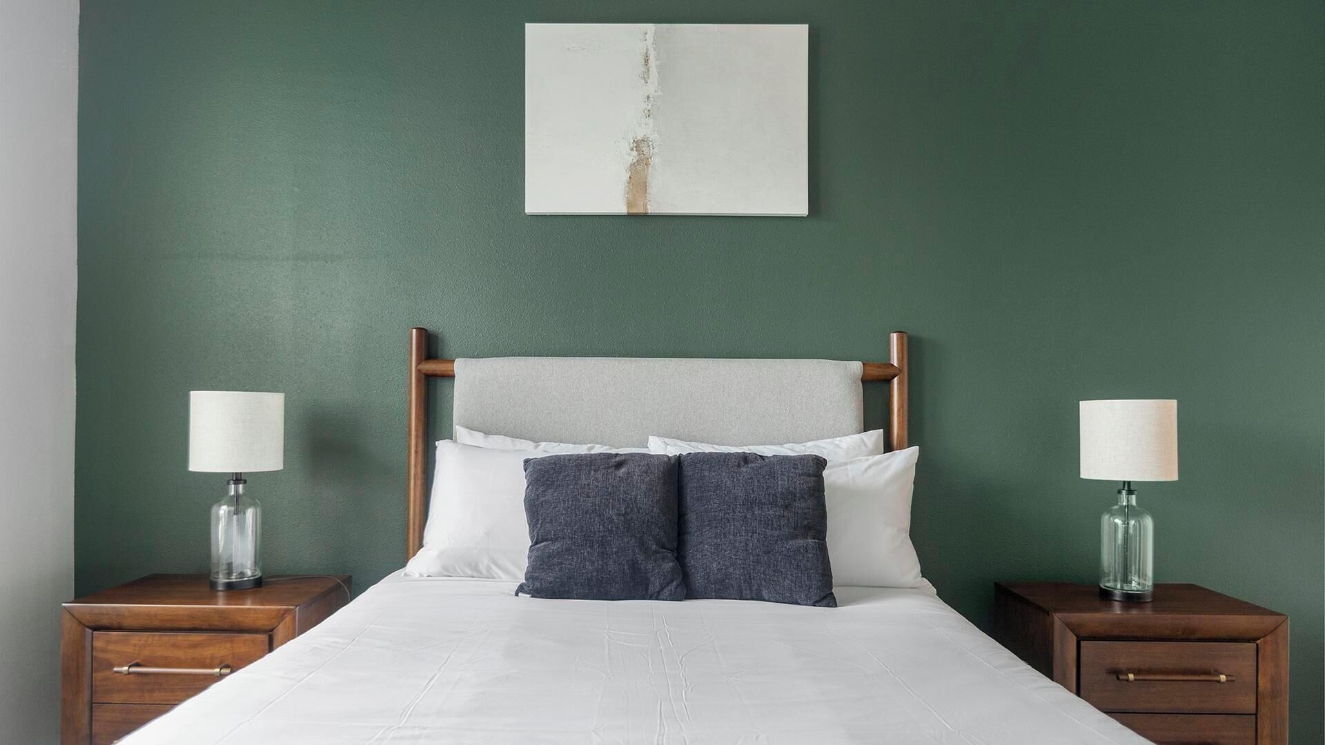 Un letto con lenzuola bianche, due comodini con lampade e una parete verde.