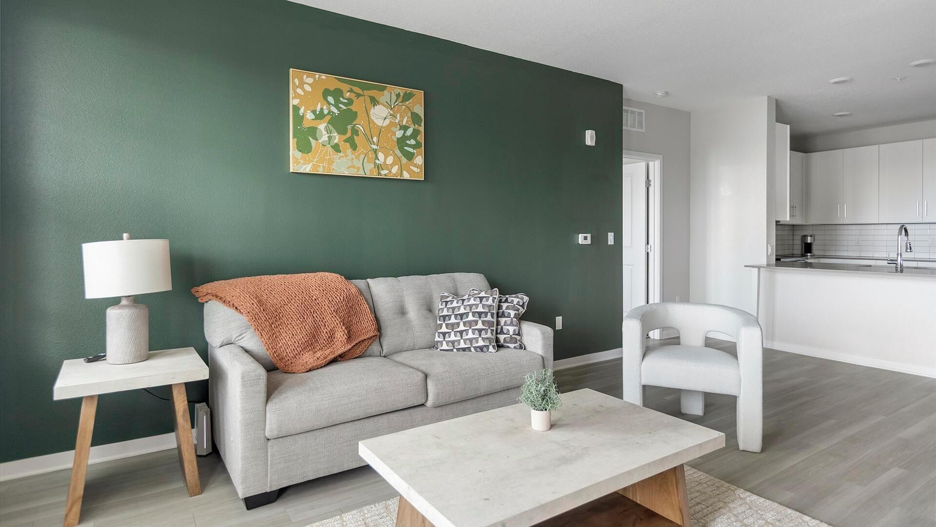 Un soggiorno con un divano grigio, un tavolino, una lampada e un quadro appeso al muro.
