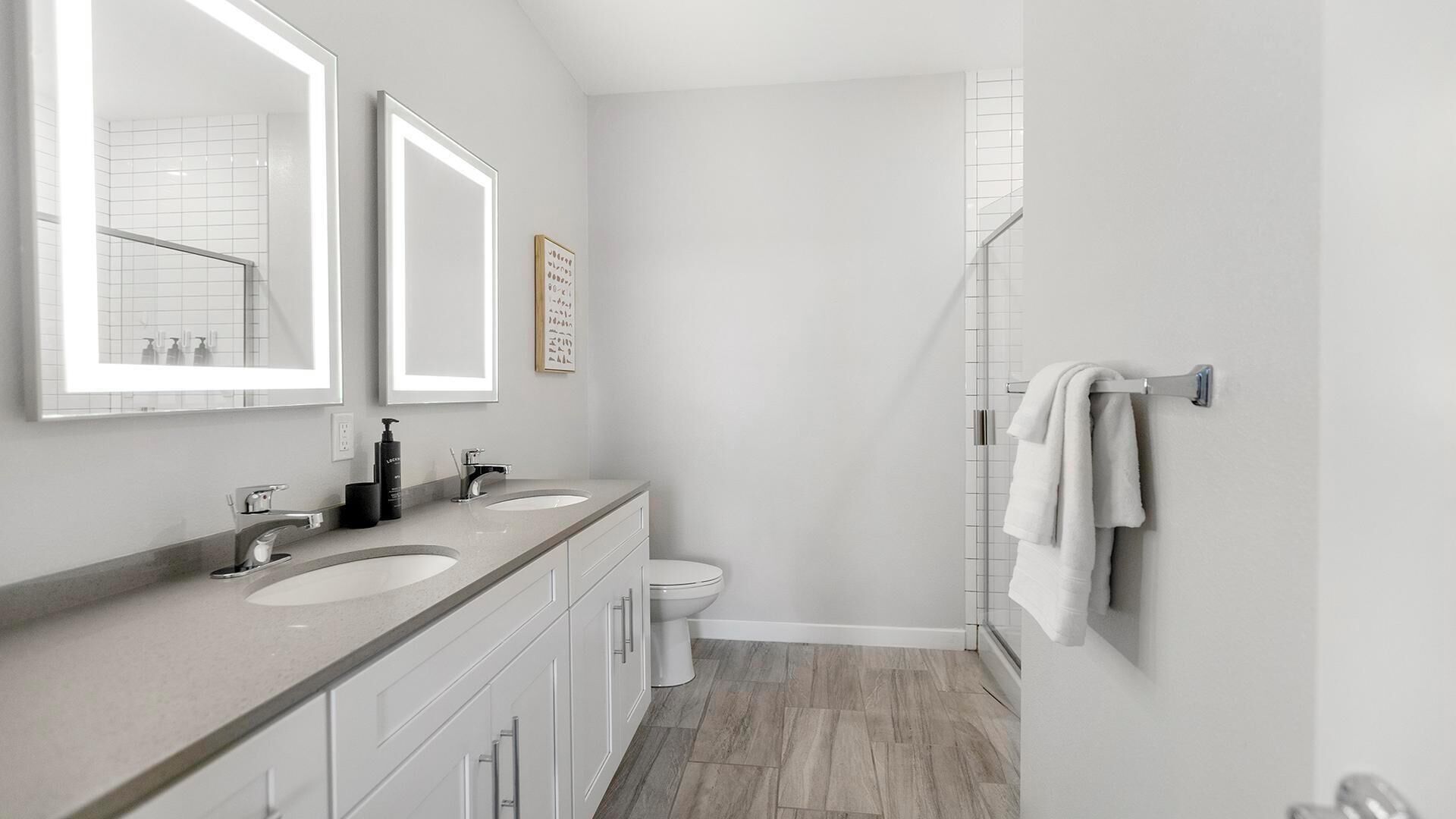Un baño moderno con dos lavamanos, un inodoro, una ducha y un perchero para toallas.