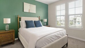 A bedroom with a bed, two bedside tables, a nightstand, a window with blinds, and a wall-mounted artwork.