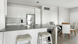 Une cuisine moderne avec des meubles blancs, un réfrigérateur en acier inoxydable et un coin bar équipé de tabourets.