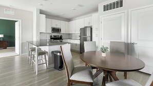 Une cuisine moderne avec des meubles blancs, des appareils en acier inoxydable, un îlot central doté de tabourets et une table à manger avec des chaises.