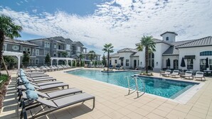 Une piscine entourée de chaises longues, de palmiers et d’un bâtiment dont le toit est recouvert de tuiles.