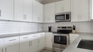 A modern kitchen with white cabinets, a stainless steel microwave, a coffee maker, and a stove. - Landing | Beautiful 2BD, Gym (Sun City Center)