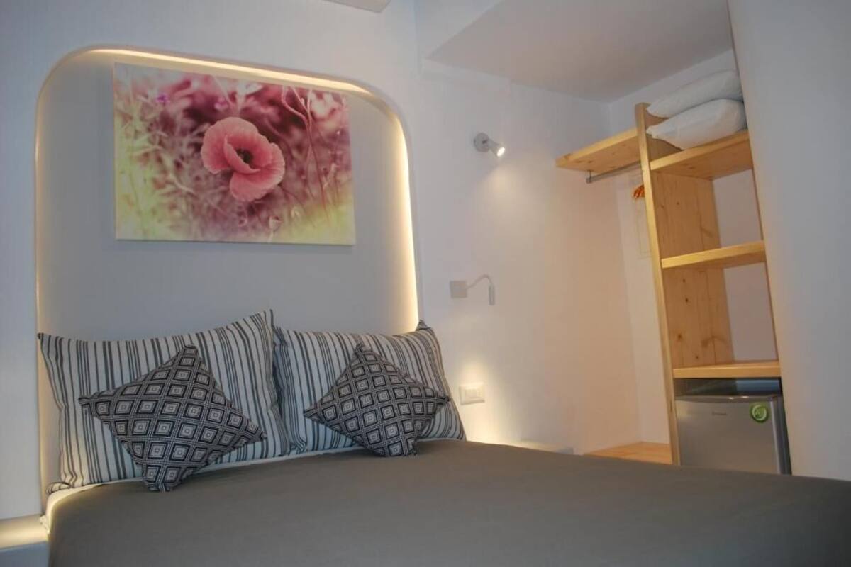 A bedroom with a bed, pillows, a wall-mounted painting, and a wooden shelf.