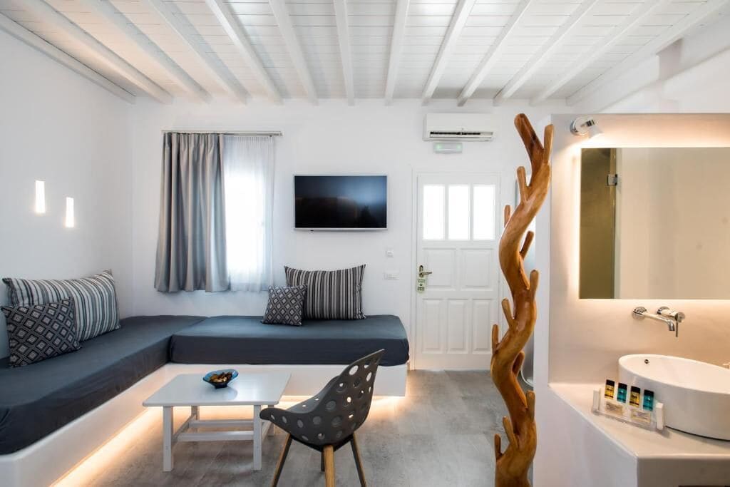Una habitación moderna con sofá, mesa de centro, televisión, baño con lavamanos y espejo, y un original adorno de madera.