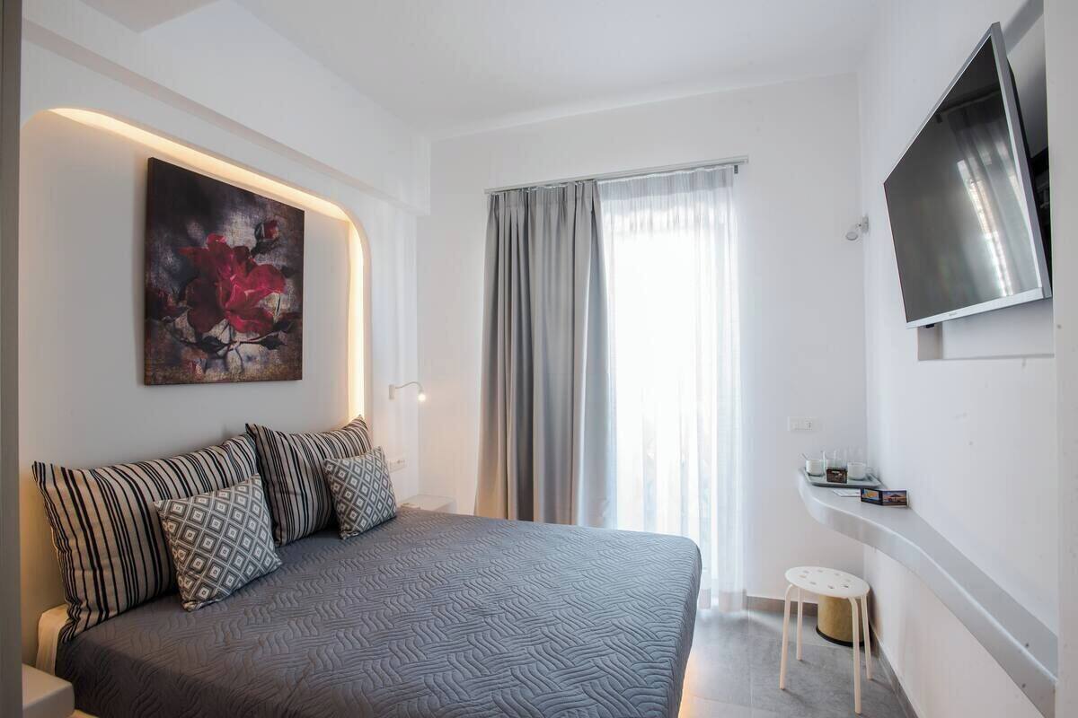 A modern bedroom with a bed, a mounted TV, a painting, and a small table.