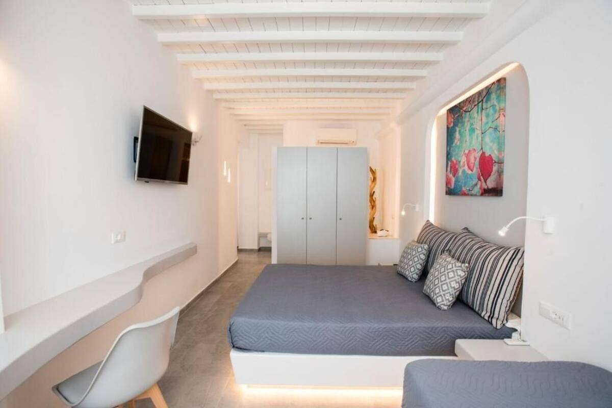 A bedroom with a bed, a chair, a TV, a wardrobe, and a painting on the wall.