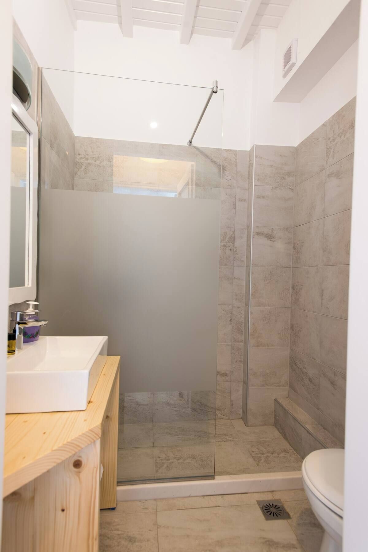 A modern bathroom with a glass-enclosed shower, a wooden vanity, and a white toilet.