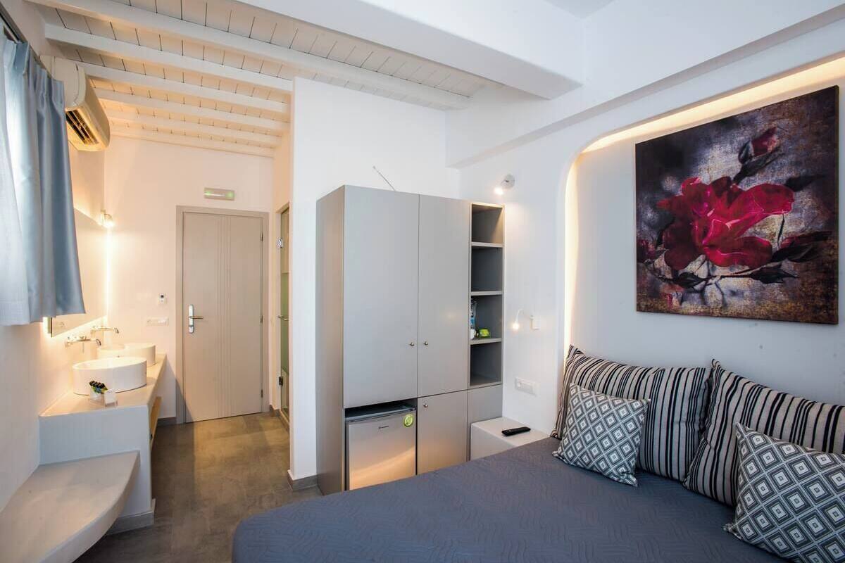 A bedroom with a bed, a bedside table, a wardrobe, a painting, and a bathroom with a sink and mirror.