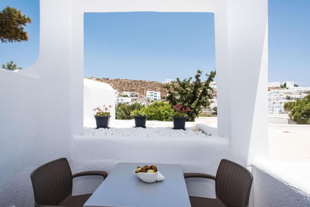 A white-walled outdoor seating area with a table and chairs, a bowl of fruit, and potted plants.