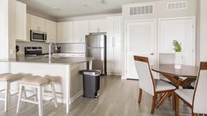 Een moderne keuken met witte kasten, roestvrijstalen apparatuur en een centraal eiland met barkrukken.