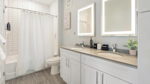 A modern bathroom with a shower, two sinks, a toilet, and a potted plant.