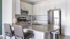 A modern kitchen with white cabinets, a stainless steel refrigerator, a microwave, and a gas stove.