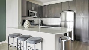 A modern kitchen with dark cabinets, stainless steel appliances, a white island with stools, and a microwave above the sink.