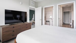 Ein Schlafzimmer mit Fernseher auf einer Kommode, einem Bett und offenen Schränken, die zu einem Badezimmer führen.