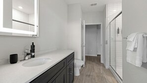 A modern bathroom with a large mirror, two sinks, a toilet, and a shower area.