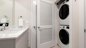 Une salle de bain moderne équipée d’un lavabo, d’un miroir, d’un porte-serviettes et de deux machines à laver superposées.