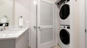 Ein modernes Badezimmer mit Waschbecken, Spiegel, Handtuchhalter und zwei gestapelten Waschmaschinen.