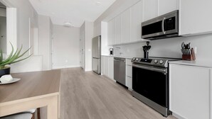 Une cuisine moderne avec des meubles blancs, des appareils en acier inoxydable et une table à manger en bois.