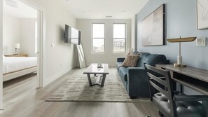 A modern living room with a sofa, coffee table, TV, and a desk with a lamp. - Landing | Modern 1BD in Columbia Heights (Washington)