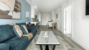 A modern living room with a sofa, coffee table, and a view into the kitchen. - Landing | Modern 1BD in Columbia Heights (Washington)