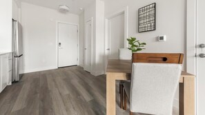 A modern kitchen with white cabinets, a wooden dining table, and a chair. - Landing | Modern 1BD in Columbia Heights (Washington)