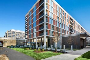 A multi-story hotel with a modern design, featuring a mix of glass and brick facade, a covered entrance, and a landscaped outdoor area. - Landing | Beautiful 1BD, Gym (Washington)