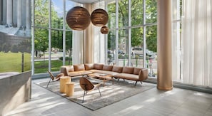 A modern lounge with a leather sofa, round wooden tables, and large windows offering a view of the outdoors. - Landing | Beautiful 1BD, Gym (Washington)