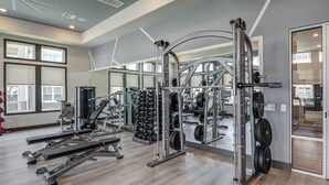 Ett modernt gym med olika typer av styrketräningsutrustning, spegelväggar och stora fönster.