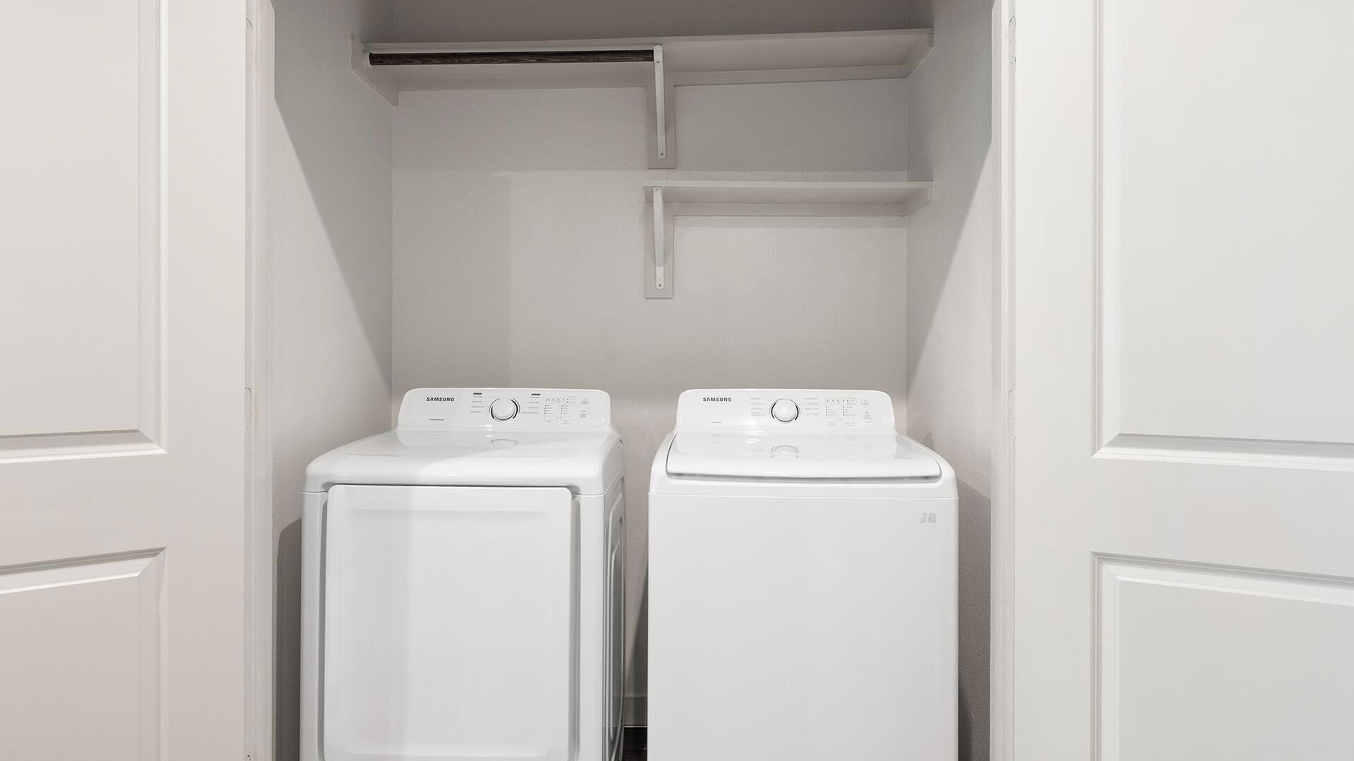 A laundry room with two white front-loading washers and dryers, a white door, and a white wall.