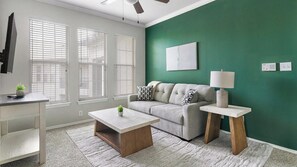 A living room with a grey sofa, a coffee table, a lamp, and a green accent wall. - Landing | Modern 1BD in Copperfield (Cypress)